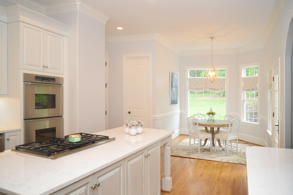 Transitional light wood floor kitchen photo with white cabinets, beige backsplash, stainless steel appliances and an island