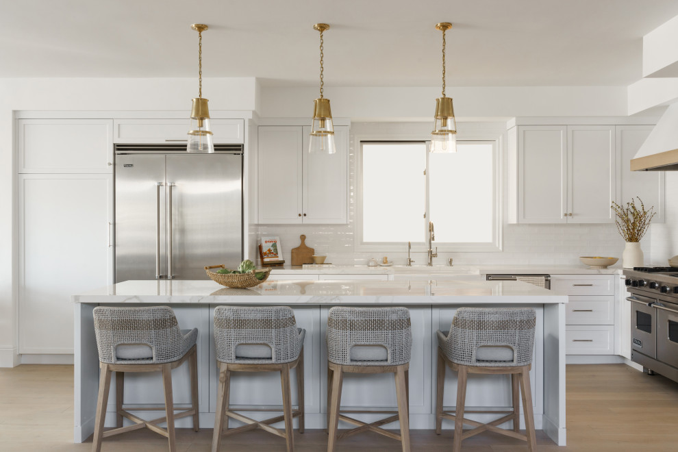 This is an example of a large beach style l-shaped open plan kitchen in Orange County with an undermount sink, recessed-panel cabinets, white cabinets, white splashback, subway tile splashback, stainless steel appliances, light hardwood floors, with island, yellow benchtop and quartzite benchtops.