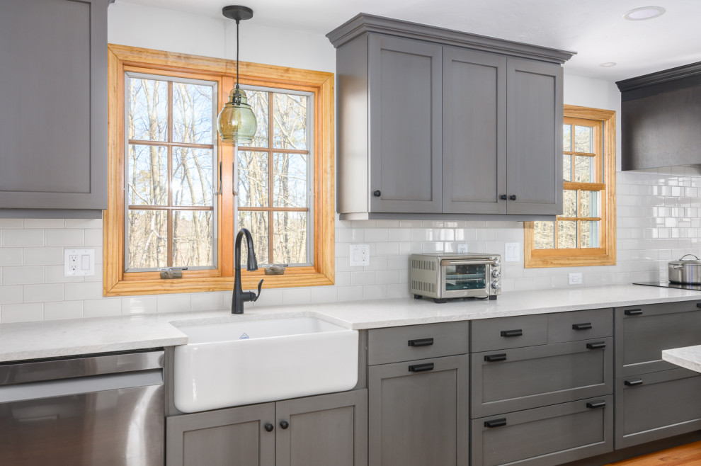 This is an example of a large traditional l-shaped eat-in kitchen in Boston with a farmhouse sink, recessed-panel cabinets, grey cabinets, quartzite benchtops, white splashback, ceramic splashback, stainless steel appliances, medium hardwood floors, with island, brown floor and white benchtop.