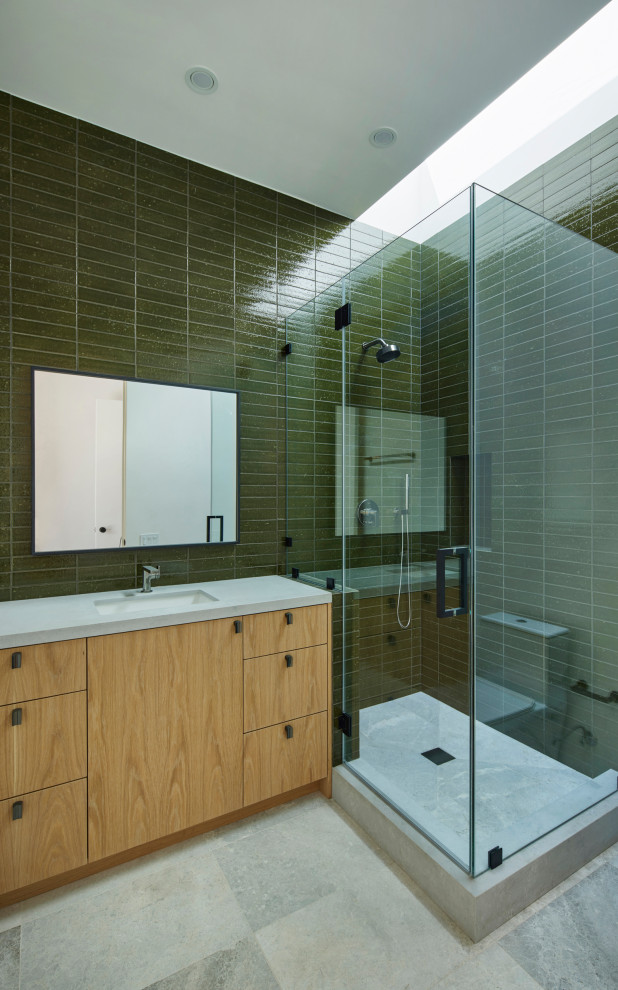 This is an example of a medium sized modern shower room bathroom in Los Angeles with freestanding cabinets, light wood cabinets, a corner shower, a one-piece toilet, green tiles, ceramic tiles, green walls, limestone flooring, a submerged sink, solid surface worktops, beige floors, a hinged door, white worktops, a wall niche, a single sink, a built in vanity unit and brick walls.