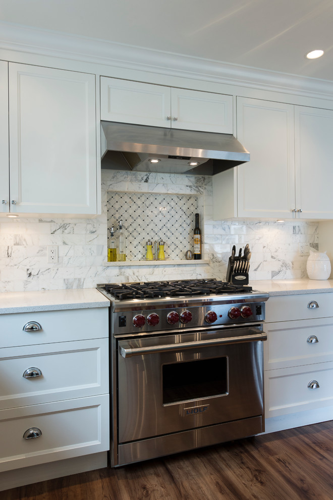 Example of a mid-sized transitional l-shaped medium tone wood floor open concept kitchen design in Vancouver with an undermount sink, shaker cabinets, white cabinets, quartz countertops, white backsplash, stone tile backsplash, stainless steel appliances and an island