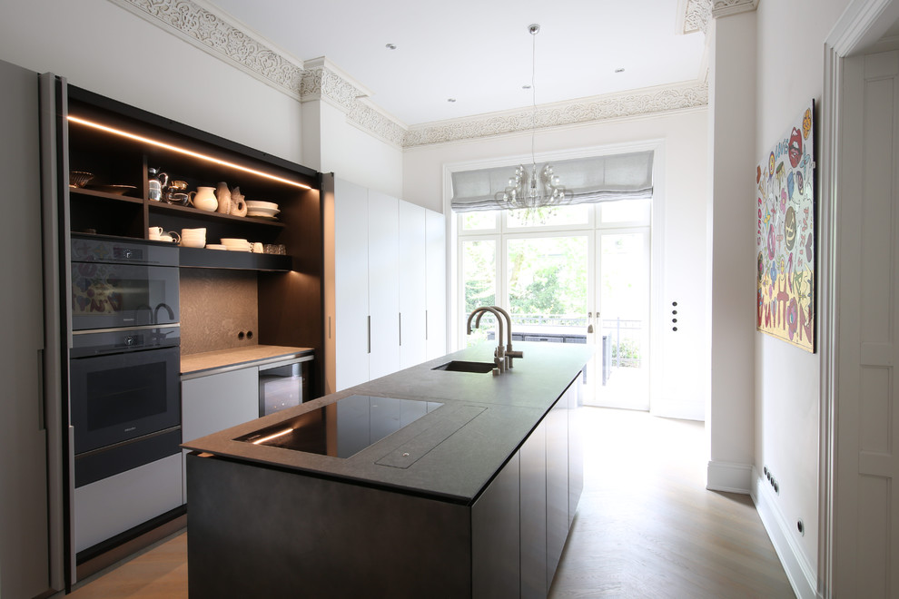 This is an example of a mid-sized contemporary single-wall separate kitchen in Hamburg with an integrated sink, flat-panel cabinets, black appliances, multiple islands, brown floor and black benchtop.