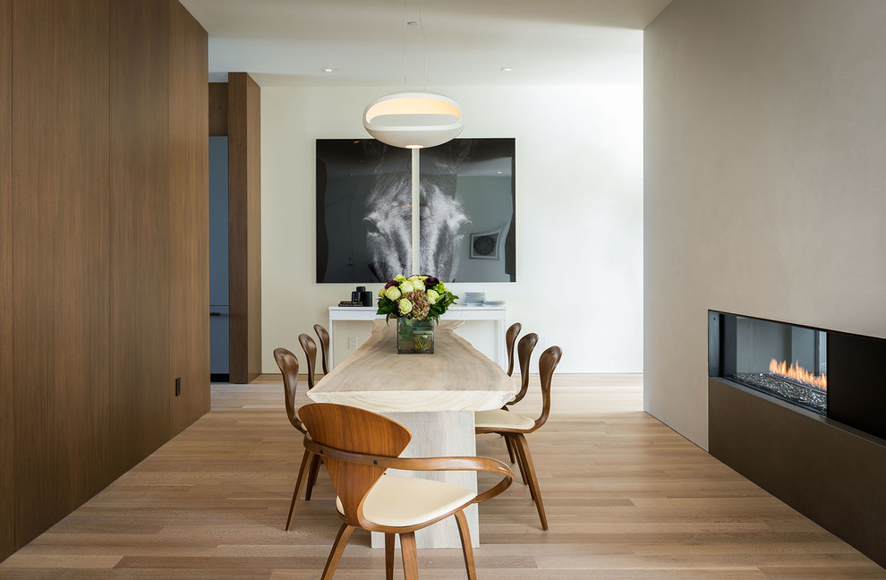 Modern dining room in San Francisco with beige walls, light hardwood floors and a two-sided fireplace.