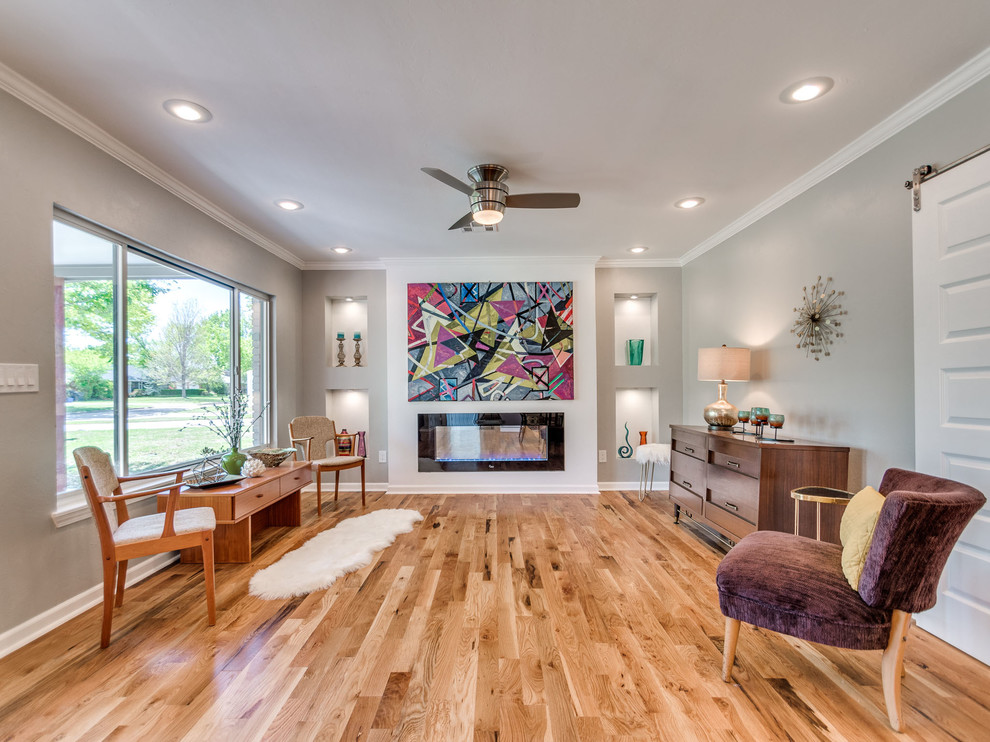 This is an example of a midcentury open concept living room in Oklahoma City with grey walls, light hardwood floors, a standard fireplace and brown floor.