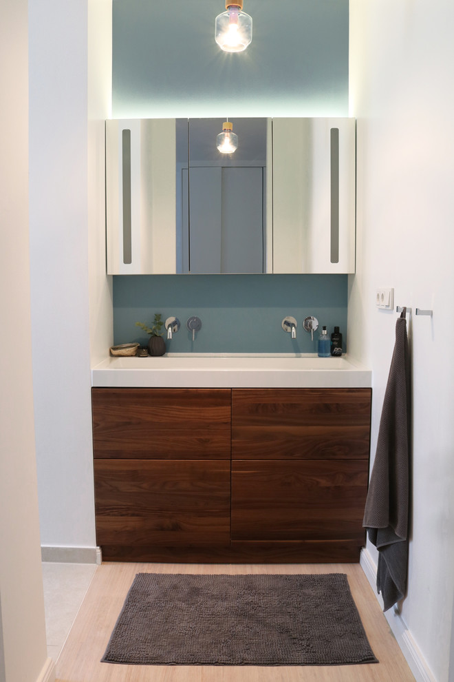 Inspiration for a mid-sized contemporary master bathroom in Berlin with flat-panel cabinets, dark wood cabinets, a drop-in tub, a wall-mount toilet, beige tile, blue walls, bamboo floors, a console sink, solid surface benchtops and white floor.