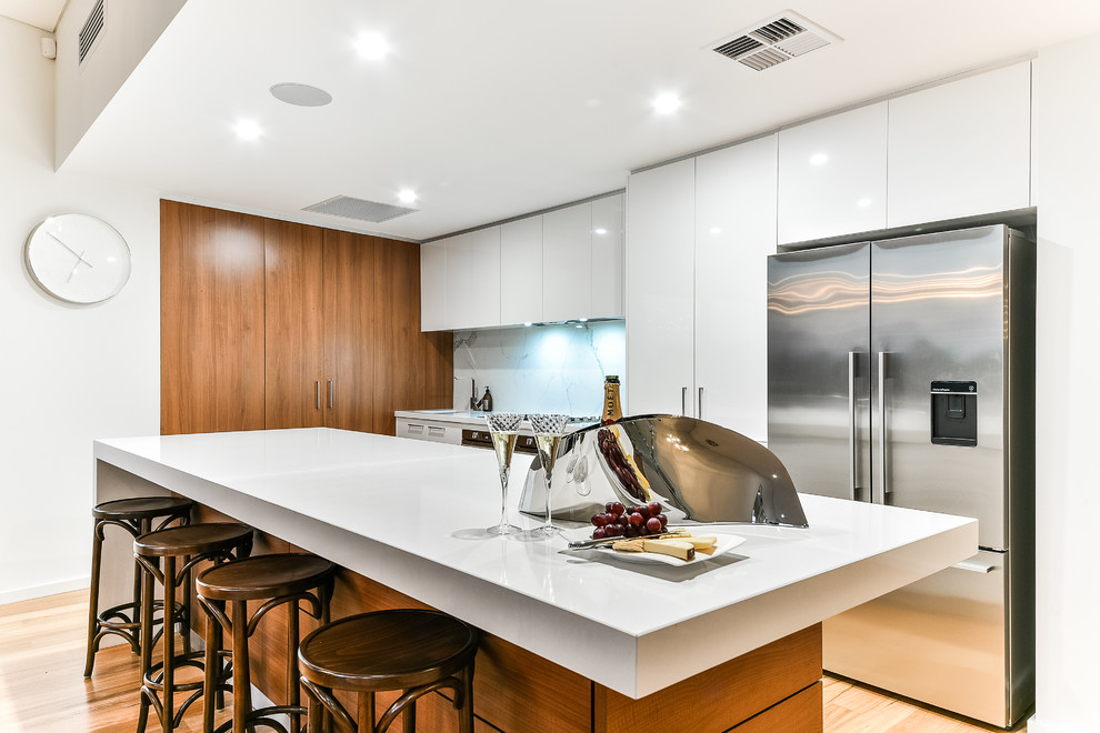 This is an example of a large contemporary galley eat-in kitchen in Perth with an undermount sink, flat-panel cabinets, white cabinets, quartz benchtops, white splashback, stone slab splashback, stainless steel appliances, with island and light hardwood floors.