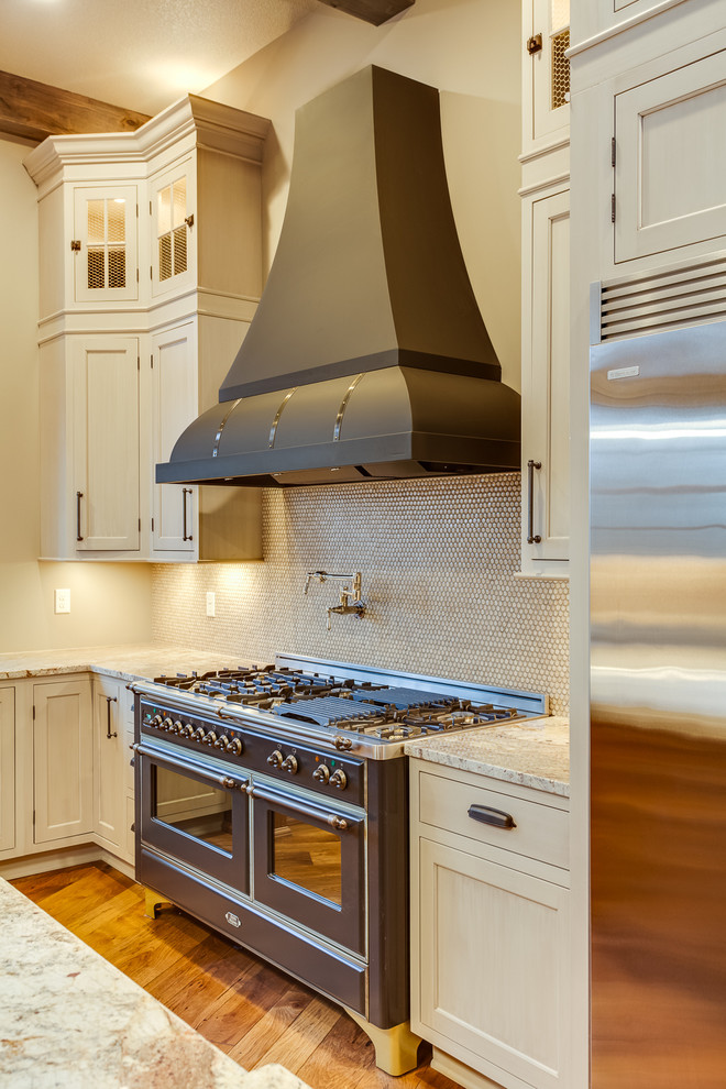 Example of a huge mountain style u-shaped medium tone wood floor eat-in kitchen design with a farmhouse sink, beaded inset cabinets, beige cabinets, granite countertops, beige backsplash, mosaic tile backsplash, stainless steel appliances and an island