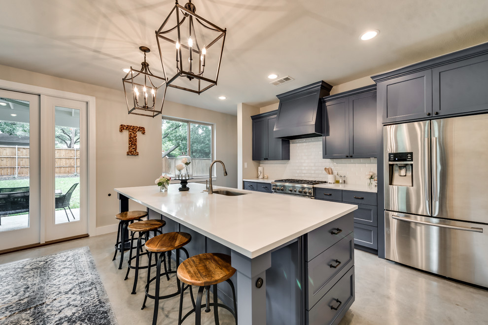 Photo of a country single-wall open plan kitchen in Dallas with an undermount sink, shaker cabinets, grey cabinets, solid surface benchtops, white splashback, subway tile splashback, stainless steel appliances, concrete floors, with island and beige floor.
