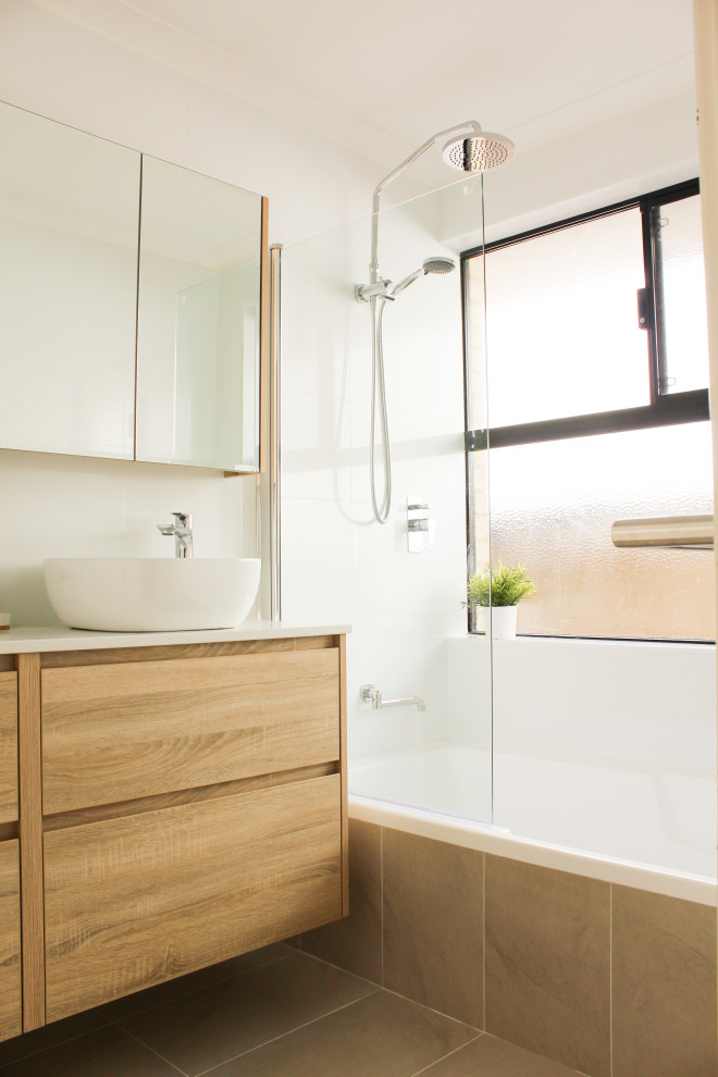 Photo of a mid-sized modern 3/4 bathroom in Perth with flat-panel cabinets, beige cabinets, a drop-in tub, a shower/bathtub combo, a one-piece toilet, white tile, ceramic tile, white walls, porcelain floors, a vessel sink, solid surface benchtops, beige floor, a hinged shower door and white benchtops.
