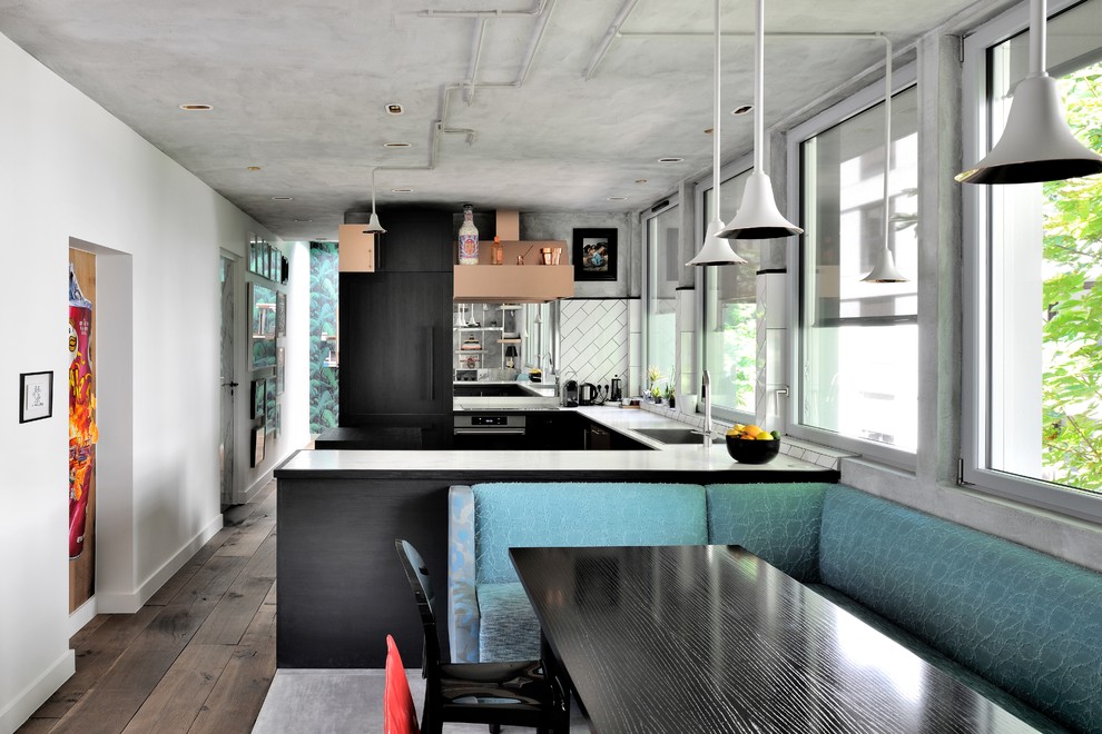 Industrial u-shaped eat-in kitchen in Other with a drop-in sink, flat-panel cabinets, black cabinets, white splashback, panelled appliances, medium hardwood floors, a peninsula, grey floor and white benchtop.
