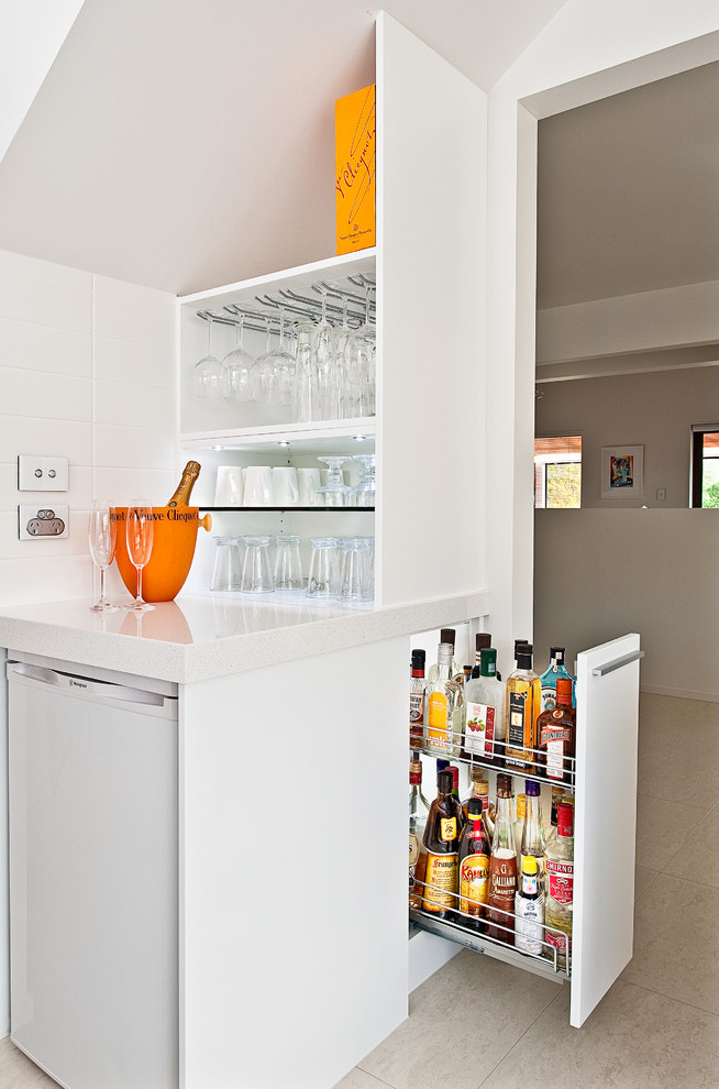 This is an example of a mid-sized contemporary u-shaped eat-in kitchen in Auckland with white cabinets, ceramic floors, an undermount sink, flat-panel cabinets, quartz benchtops, white splashback, subway tile splashback, stainless steel appliances, a peninsula and beige floor.