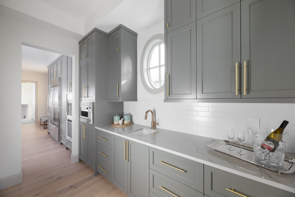 Large transitional single-wall light wood floor kitchen pantry photo in Calgary with an undermount sink, shaker cabinets, gray cabinets, quartzite countertops, gray backsplash, stainless steel appliances, an island and gray countertops