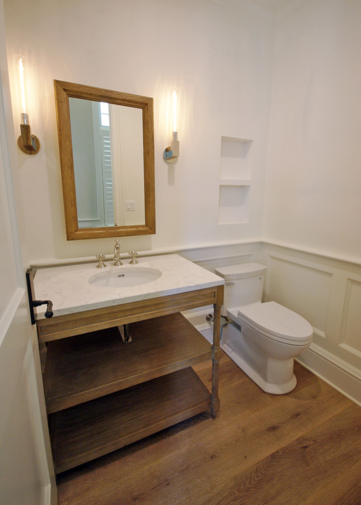 Photo of a mid-sized tropical powder room in Miami with open cabinets, light wood cabinets, a one-piece toilet, white walls, medium hardwood floors, an undermount sink, marble benchtops, brown floor and white benchtops.