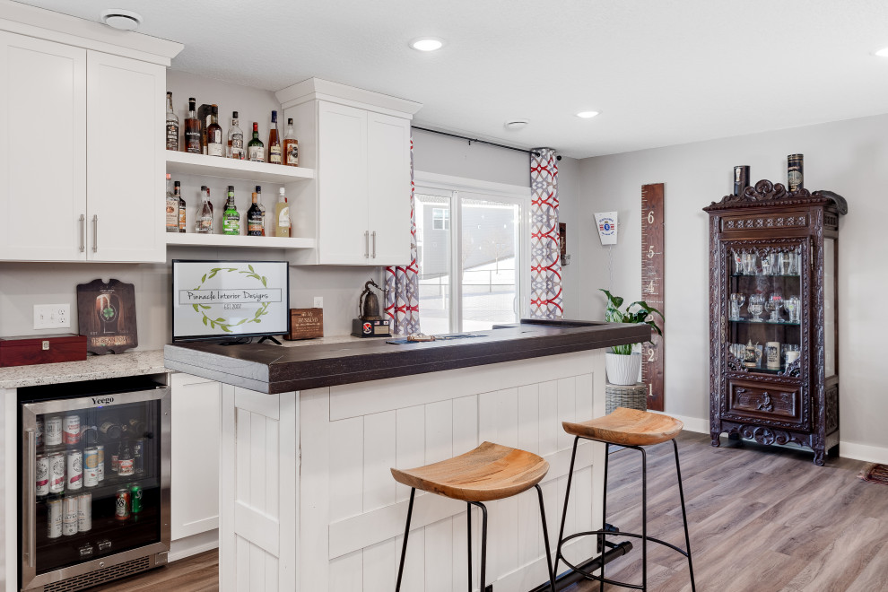Photo of a mid-sized transitional galley home bar in Other with shaker cabinets, white cabinets, wood benchtops, vinyl floors, brown floor and beige benchtop.