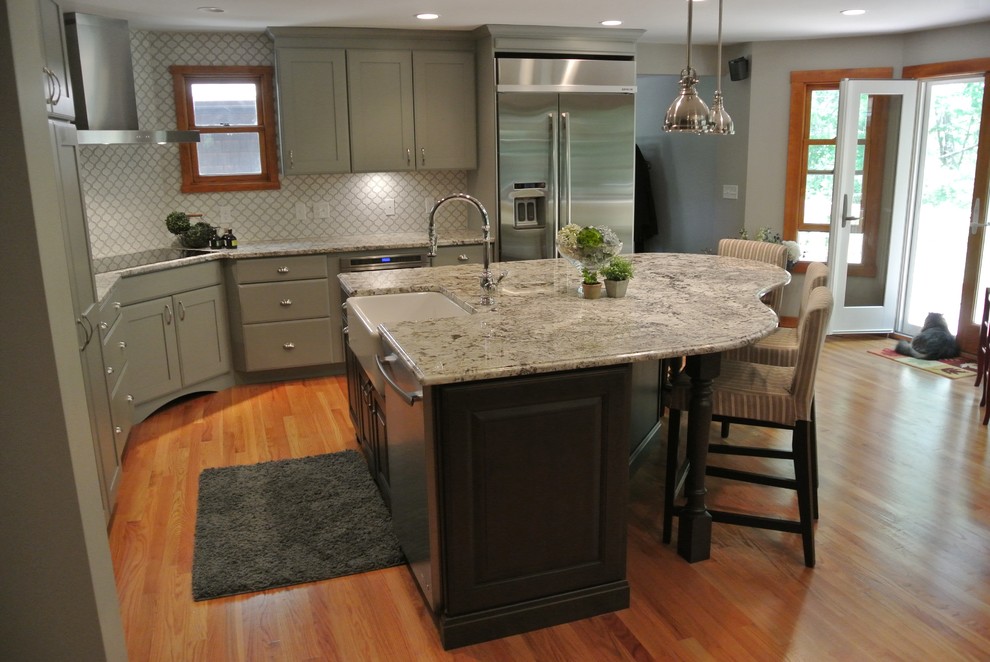 Inspiration for a large transitional l-shaped light wood floor eat-in kitchen remodel in Boston with a farmhouse sink, shaker cabinets, gray cabinets, granite countertops, white backsplash, ceramic backsplash, stainless steel appliances, an island and gray countertops