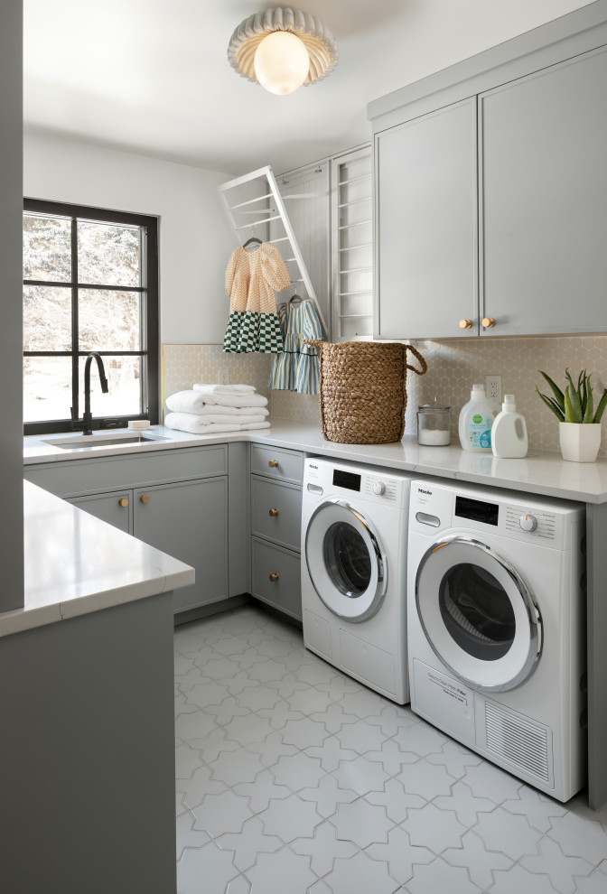 Inredning av en klassisk u-formad tvättstuga, med grå skåp och en tvättmaskin och torktumlare bredvid varandra