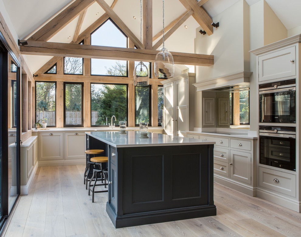 Photo of a traditional u-shaped kitchen in Buckinghamshire with beaded inset cabinets, quartzite benchtops, light hardwood floors, with island, grey cabinets, black appliances, beige floor and grey benchtop.