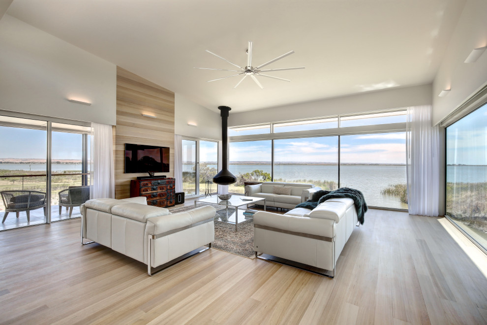 Contemporary open concept living room in Adelaide with white walls, light hardwood floors, a hanging fireplace, a wall-mounted tv and beige floor.