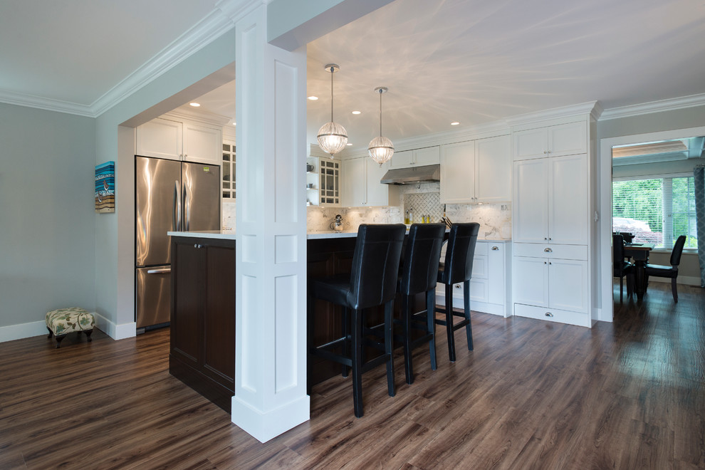 Inspiration for a mid-sized transitional l-shaped medium tone wood floor open concept kitchen remodel in Vancouver with an undermount sink, shaker cabinets, white cabinets, quartz countertops, white backsplash, stone tile backsplash, stainless steel appliances and an island