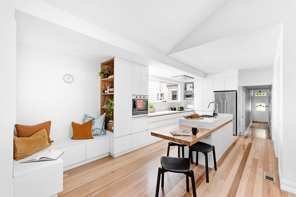 メルボルンにある高級な中くらいなコンテンポラリースタイルのおしゃれなキッチン (白いキャビネット、白いキッチンパネル、シルバーの調理設備、黄色いキッチンカウンター、ダブルシンク、三角天井) の写真