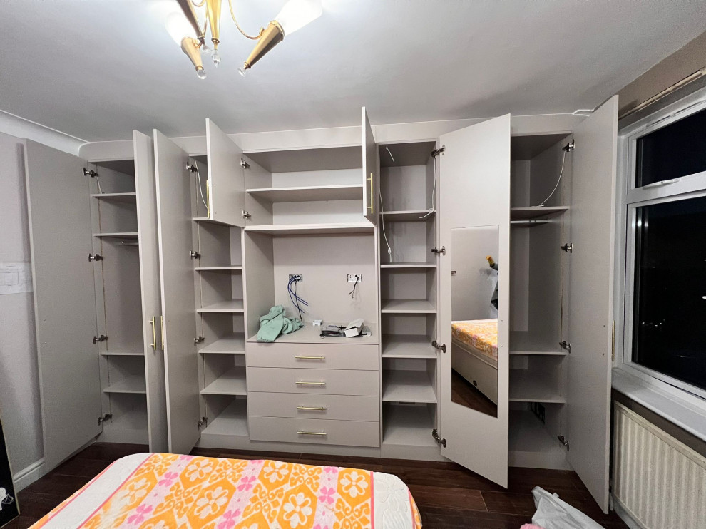This is an example of a mid-sized traditional gender-neutral storage and wardrobe in London with flat-panel cabinets, white cabinets, laminate floors, brown floor and recessed.