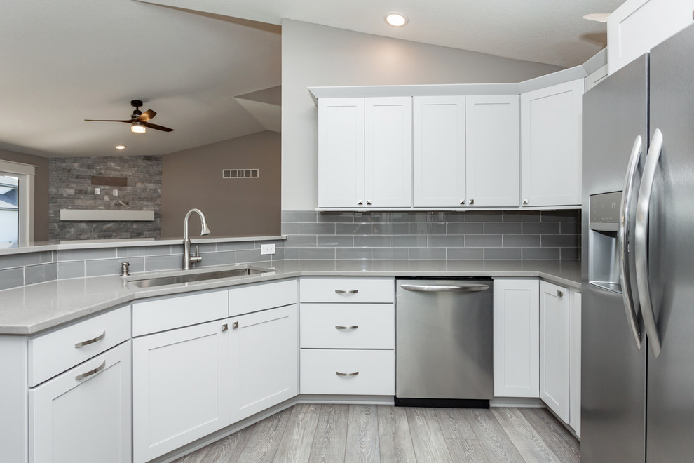 Example of a mid-sized transitional u-shaped medium tone wood floor and gray floor kitchen design with an undermount sink, shaker cabinets, white cabinets, quartz countertops, gray backsplash, ceramic backsplash, stainless steel appliances, no island and gray countertops