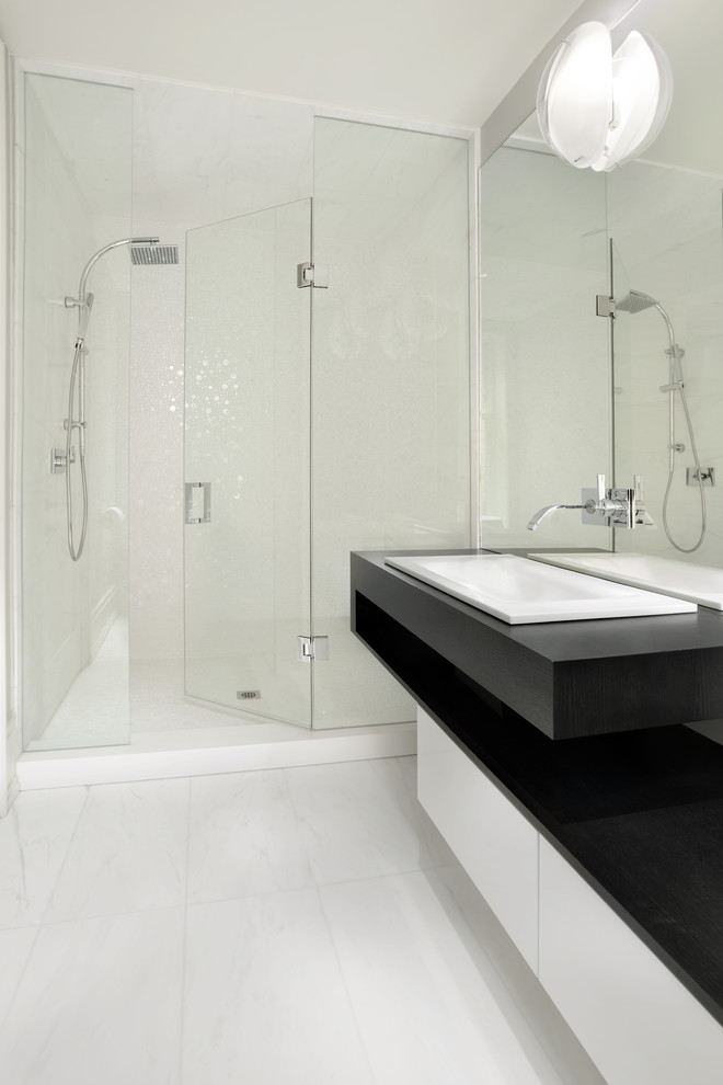 This is an example of a mid-sized contemporary 3/4 bathroom in Toronto with a drop-in sink, flat-panel cabinets, white cabinets, an alcove shower, white tile, marble floors, solid surface benchtops, white floor and black benchtops.