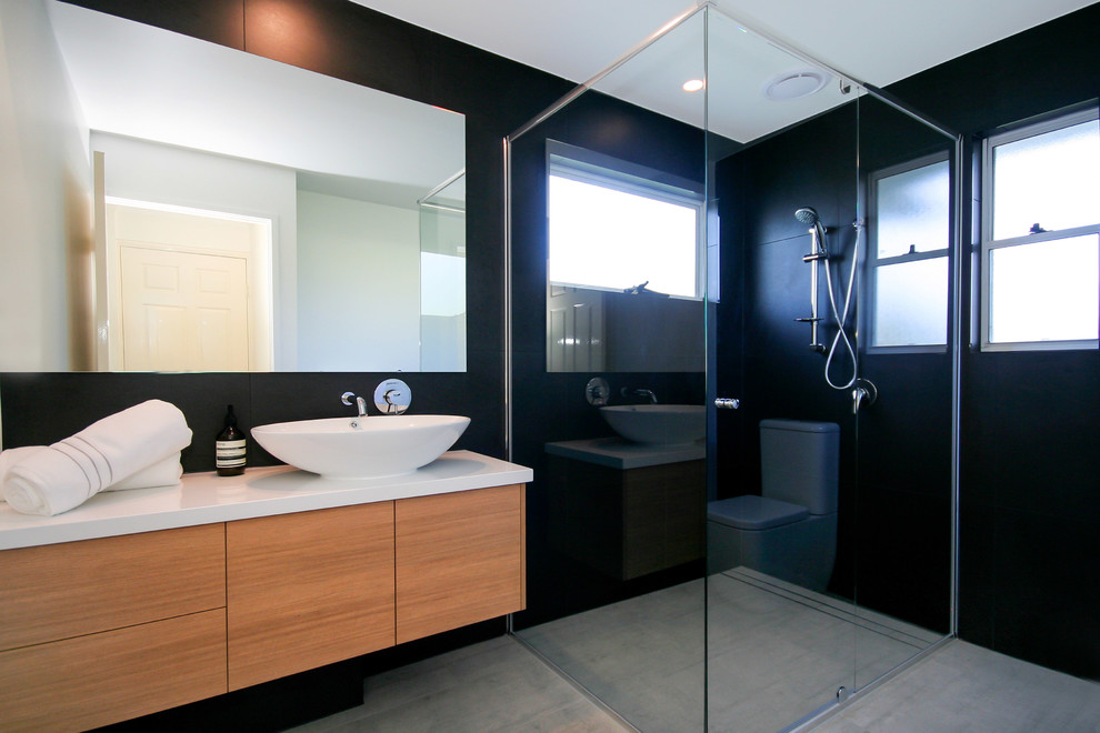 This is an example of a mid-sized modern 3/4 bathroom in Sunshine Coast with a corner shower, a one-piece toilet, gray tile, ceramic tile, black walls, ceramic floors, a vessel sink, engineered quartz benchtops, flat-panel cabinets and light wood cabinets.