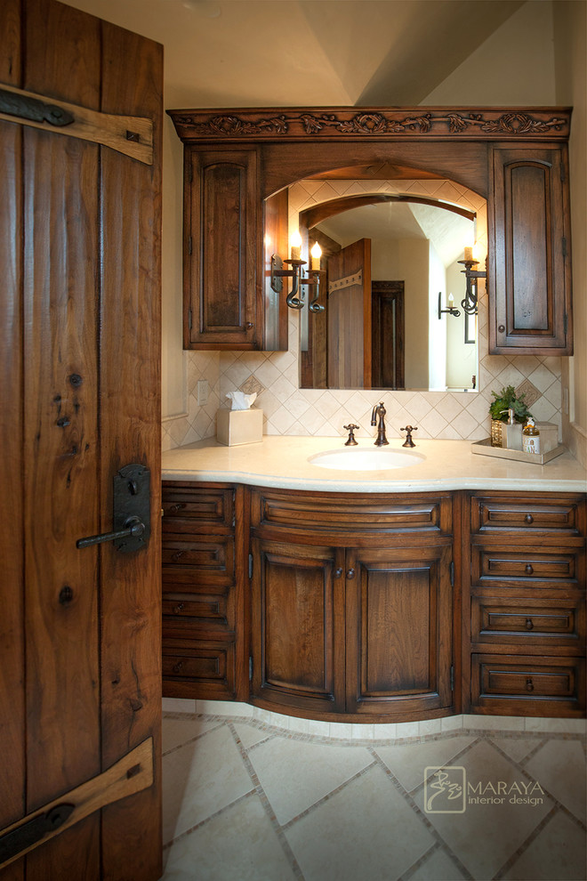 Design ideas for a mid-sized country bathroom in Santa Barbara with raised-panel cabinets, dark wood cabinets, a freestanding tub, beige tile, stone tile, an undermount sink and limestone benchtops.