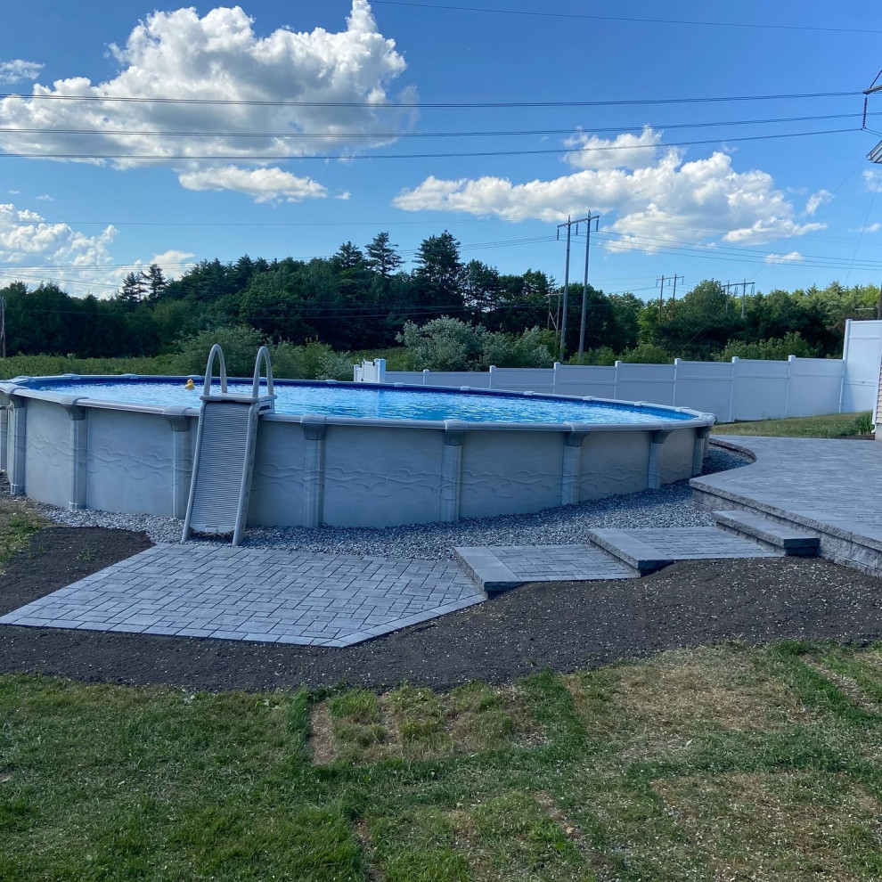 Ejemplo de piscina elevada de tamaño medio redondeada en patio trasero con paisajismo de piscina y adoquines de hormigón