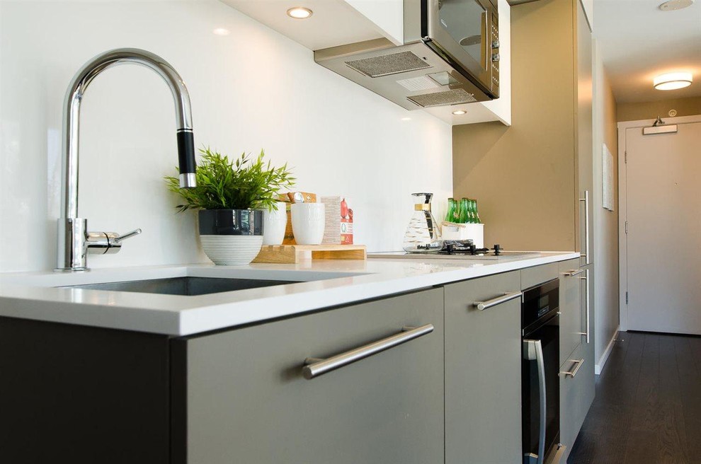 This is an example of a small contemporary single-wall open plan kitchen in Vancouver with an undermount sink, flat-panel cabinets, grey cabinets, quartz benchtops, white splashback, stone slab splashback, stainless steel appliances and dark hardwood floors.