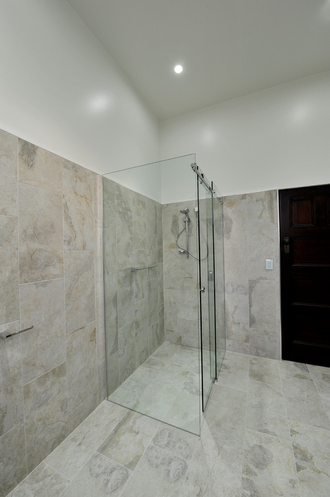 This is an example of a mid-sized contemporary master bathroom in Melbourne with beige cabinets, a double shower, a two-piece toilet, beige tile, stone slab, beige walls, porcelain floors, an undermount sink and glass benchtops.