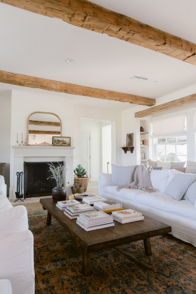 Example of a large country enclosed light wood floor, brown floor and exposed beam living room design in Dallas with white walls, a standard fireplace and a wall-mounted tv