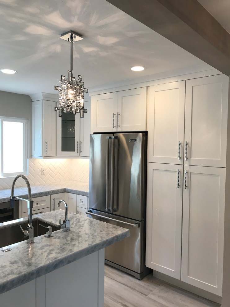 Large transitional u-shaped open plan kitchen in San Diego with an undermount sink, shaker cabinets, white cabinets, quartz benchtops, white splashback, ceramic splashback, stainless steel appliances, porcelain floors, with island, grey floor and grey benchtop.