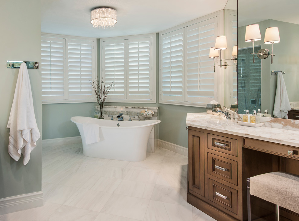 Photo of a large transitional master bathroom in Miami with a drop-in sink, raised-panel cabinets, medium wood cabinets, marble benchtops, a freestanding tub, white tile, stone slab, blue walls and marble floors.