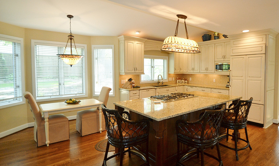 Inspiration for a large transitional l-shaped medium tone wood floor eat-in kitchen remodel in Columbus with an undermount sink, raised-panel cabinets, beige cabinets, granite countertops, beige backsplash, paneled appliances and an island