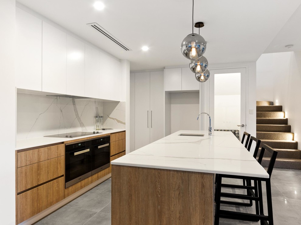 Design ideas for a mid-sized contemporary galley open plan kitchen in Perth with flat-panel cabinets, marble benchtops, white splashback, marble splashback, black appliances, ceramic floors, with island, grey floor, white benchtop, an undermount sink and medium wood cabinets.