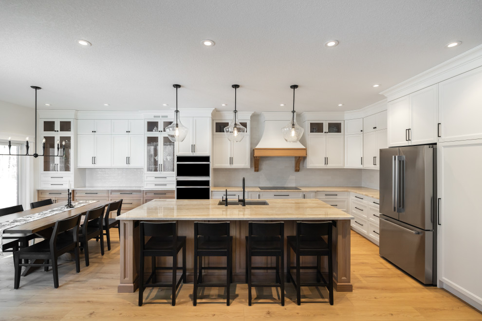 Eat-in kitchen - large transitional l-shaped light wood floor and brown floor eat-in kitchen idea in Toronto with an undermount sink, shaker cabinets, white cabinets, quartzite countertops, white backsplash, ceramic backsplash, stainless steel appliances, an island and beige countertops