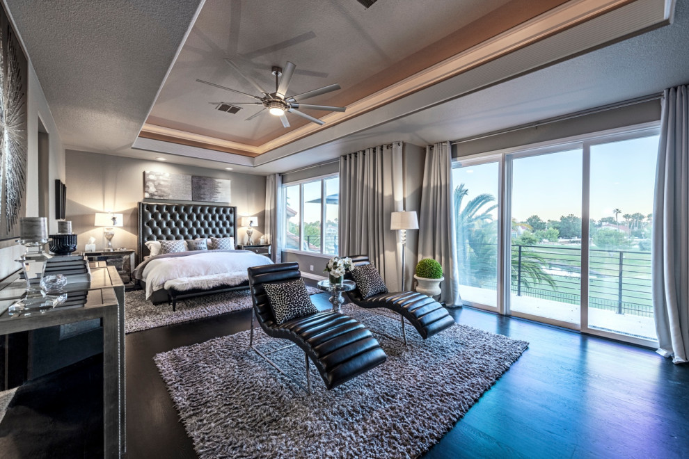 This is an example of a large transitional master bedroom in Las Vegas with grey walls, dark hardwood floors, a two-sided fireplace, a tile fireplace surround and black floor.