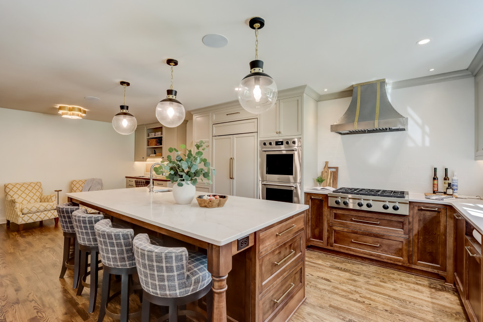 Example of a mid-sized transitional l-shaped medium tone wood floor and brown floor enclosed kitchen design in Milwaukee with an undermount sink, recessed-panel cabinets, medium tone wood cabinets, quartz countertops, white backsplash, ceramic backsplash, stainless steel appliances, an island and white countertops