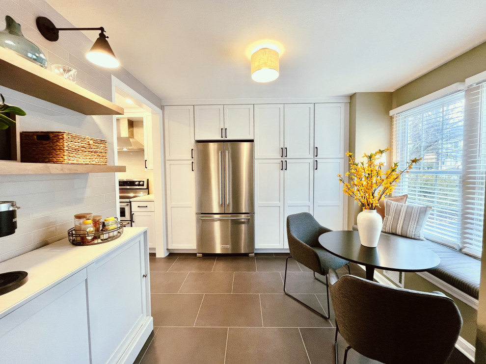 Mid-sized transitional l-shaped vinyl floor and black floor eat-in kitchen photo with a farmhouse sink, shaker cabinets, white cabinets, quartz countertops, gray backsplash, ceramic backsplash, stainless steel appliances, a peninsula and gray countertops