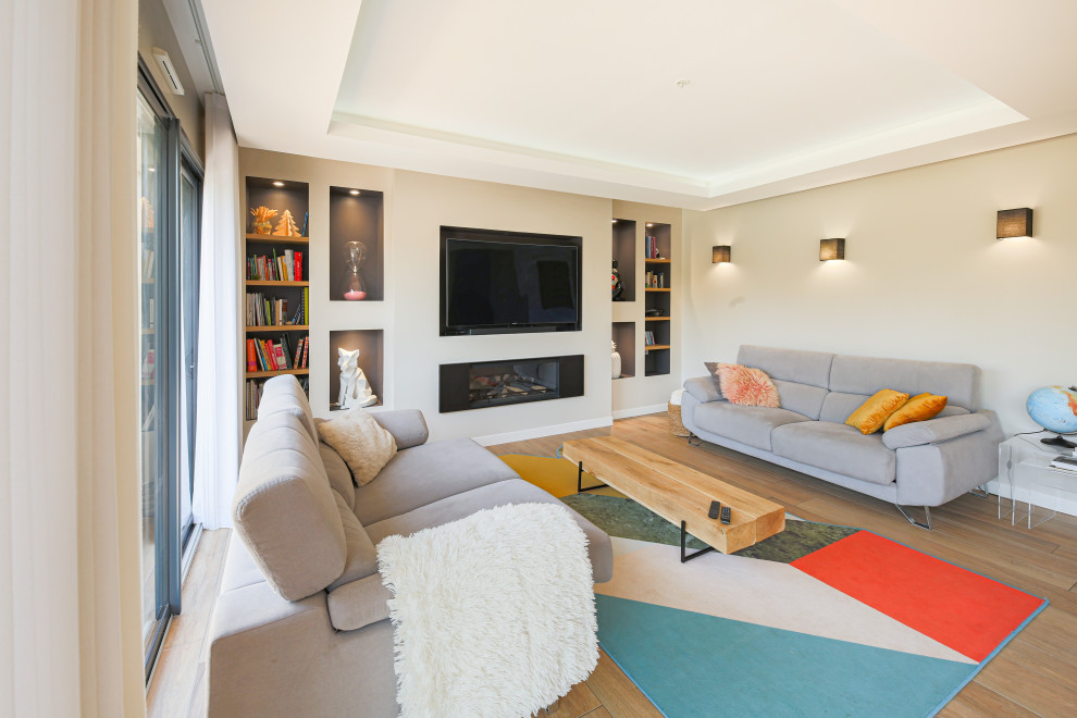 Idée de décoration pour un grand salon design ouvert avec une bibliothèque ou un coin lecture, un mur beige, parquet clair, un téléviseur encastré, un sol marron et éclairage.