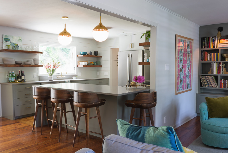 This is an example of a mid-sized midcentury l-shaped eat-in kitchen in Austin with a peninsula, flat-panel cabinets, grey cabinets, quartz benchtops, white splashback, ceramic splashback, stainless steel appliances, an undermount sink and medium hardwood floors.