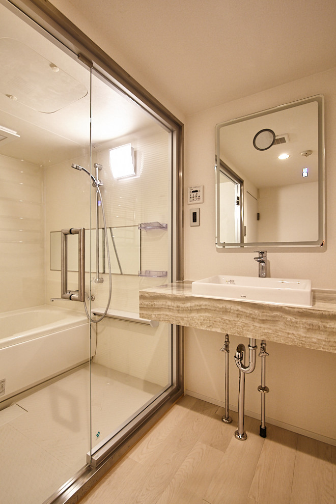 This is an example of a mid-sized contemporary master wet room bathroom in Tokyo with plywood floors, beige floor, wallpaper, wallpaper, white cabinets, a corner tub, white walls, a vessel sink, marble benchtops, a hinged shower door, beige benchtops, a single vanity and a built-in vanity.
