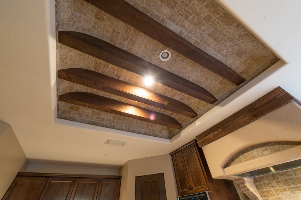 Example of a large mountain style slate floor eat-in kitchen design in Phoenix with a farmhouse sink, raised-panel cabinets, dark wood cabinets, granite countertops, beige backsplash, stone tile backsplash, paneled appliances and an island