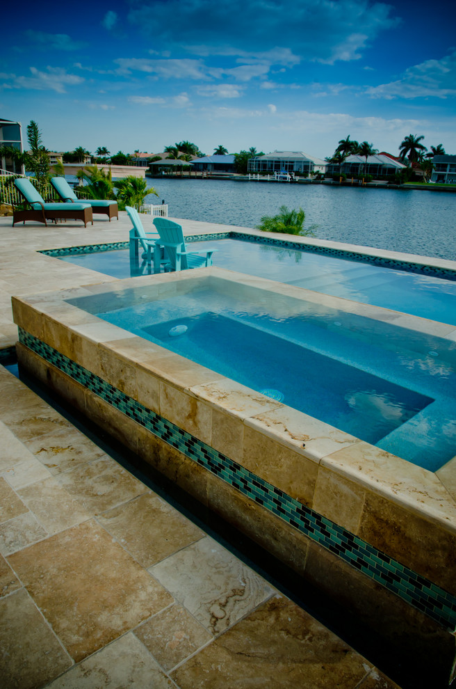 This is an example of a large beach style backyard custom-shaped pool in Miami with a pool house and natural stone pavers.