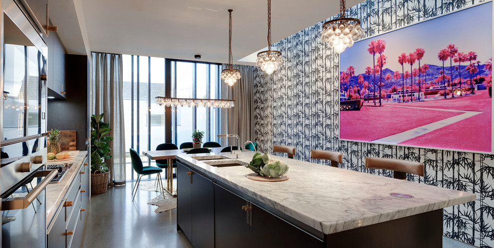 Photo of a mid-sized eclectic single-wall eat-in kitchen in Dublin with a double-bowl sink, flat-panel cabinets, black cabinets, marble benchtops, white splashback, marble splashback, coloured appliances, concrete floors, with island, grey floor and black benchtop.