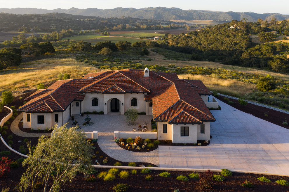 This is an example of a large mediterranean one-storey stucco beige house exterior in San Luis Obispo with a hip roof, a tile roof and a red roof.