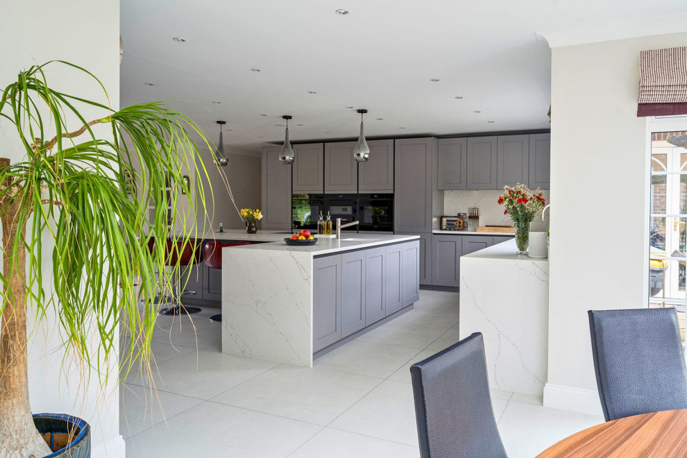 Medium sized traditional l-shaped open plan kitchen in Oxfordshire with a single-bowl sink, recessed-panel cabinets, grey cabinets, marble worktops, black appliances, an island, grey floors and white worktops.
