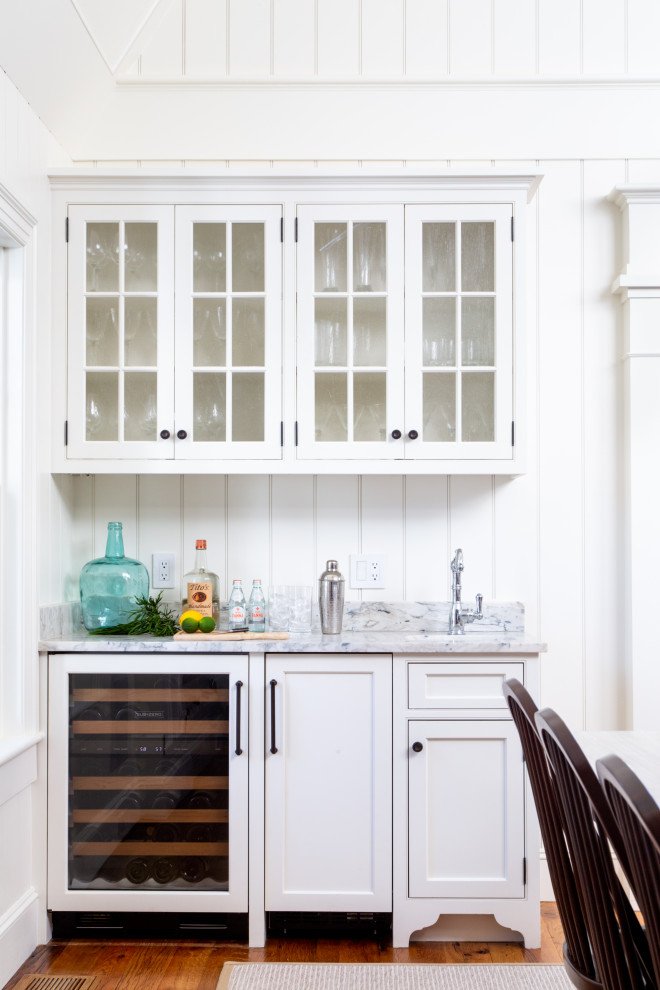 Design ideas for a beach style single-wall wet bar in Boston with white cabinets, marble benchtops, white splashback, shiplap splashback, medium hardwood floors, brown floor and white benchtop.